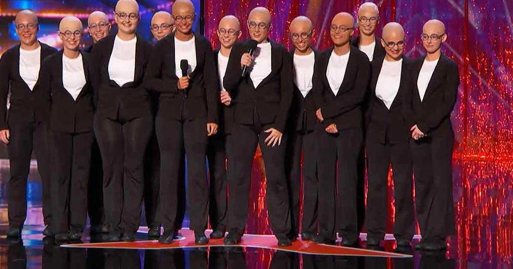 Young adult male performers in black suits and white shirts on a vibrant stage illuminated by red and blue lights during an evening performance.