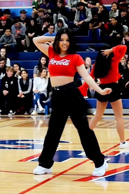 Young adult female dancers practicing in a gymnasium with an engaged audience wearing casual attire.