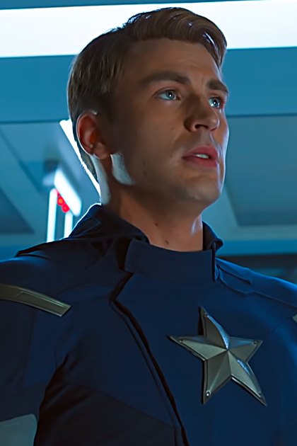 A superhero in a blue costume with silver star emblem, standing inside a high-tech facility.
