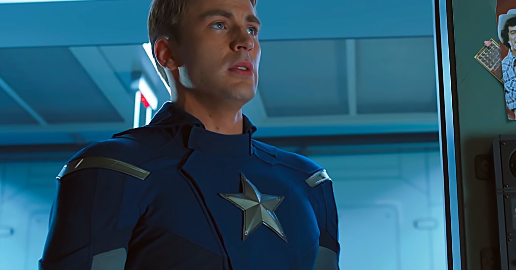 A superhero in a blue costume with silver star emblem, standing inside a high-tech facility.