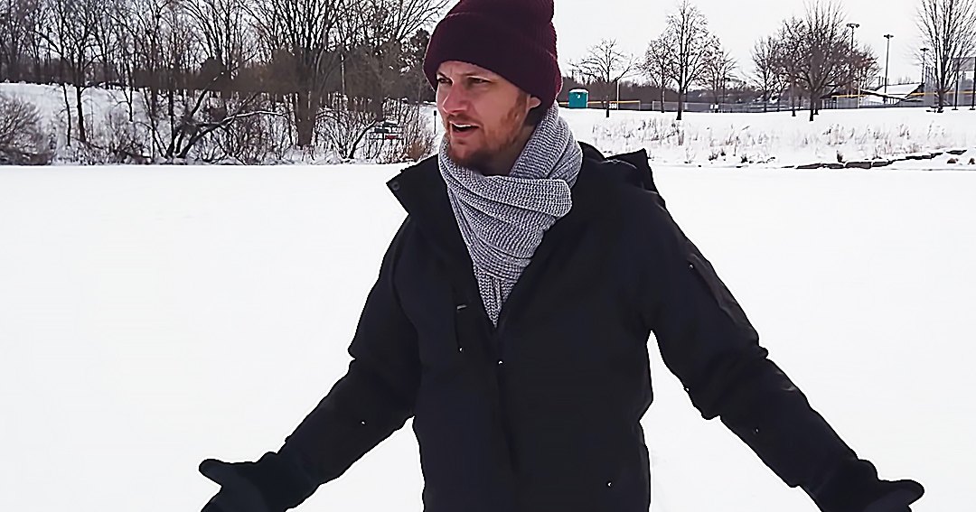 A young adult male wearing a dark jacket and scarf in a snowy outdoor setting during winter.