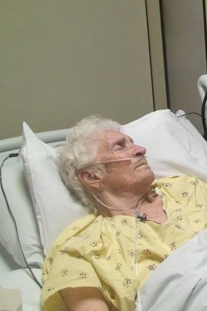 Elderly female in a hospital room with yellow floral-patterned gown, young male doctor in dark blue scrubs, modern medical equipment, indoor setting