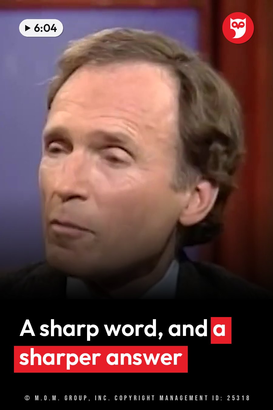 A man with brown hair in a suit and tie sits indoors near red curtains, looking slightly to his left. A headline runs in white letters across the lower third.
