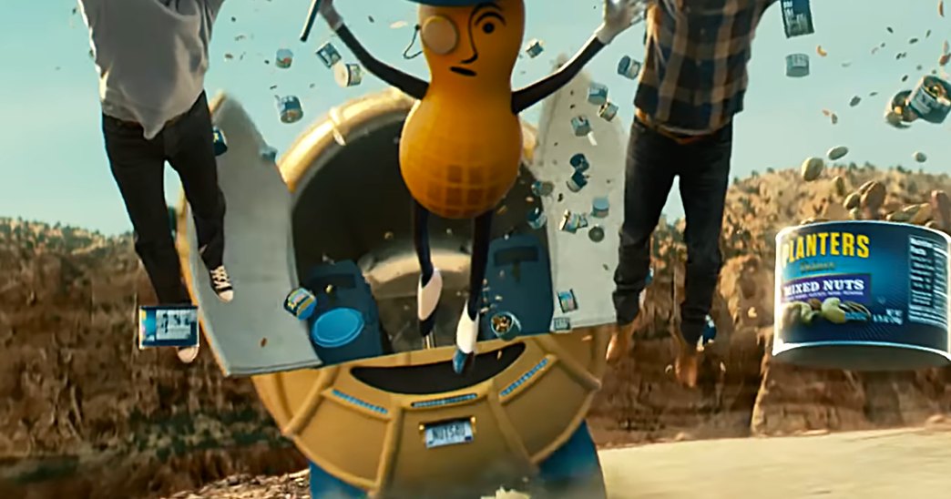 A peanut character in a top hat stands outdoors among scattered Planters Mixed Nuts cans against a desert-like rocky terrain with clear skies.