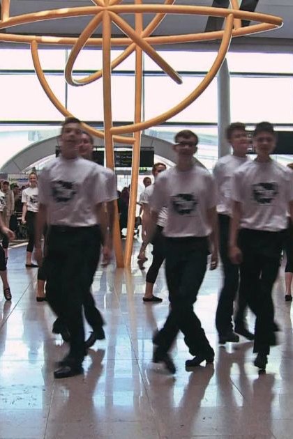 Young adults performing synchronized dance steps in a modern airport terminal with golden sculpture and directional signs visible.