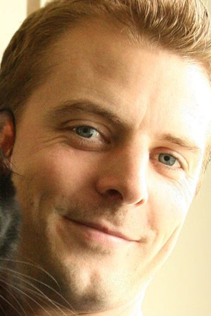 An adult male holding a black cat with yellow eyes indoors, soft natural lighting creates a warm atmosphere