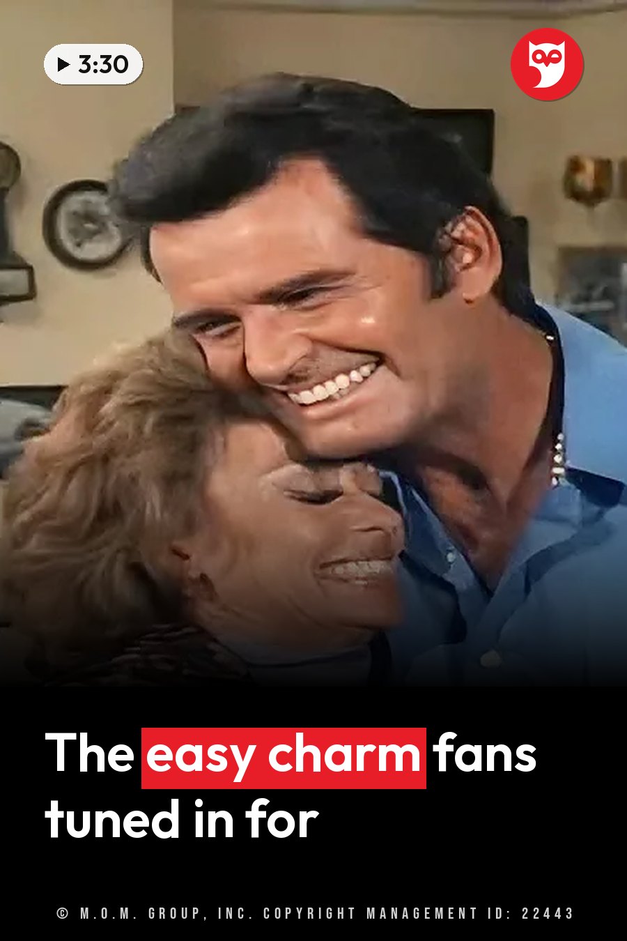A smiling man and woman hug closely indoors, with a clock on the wall behind them. A headline runs in white letters across the lower third.
