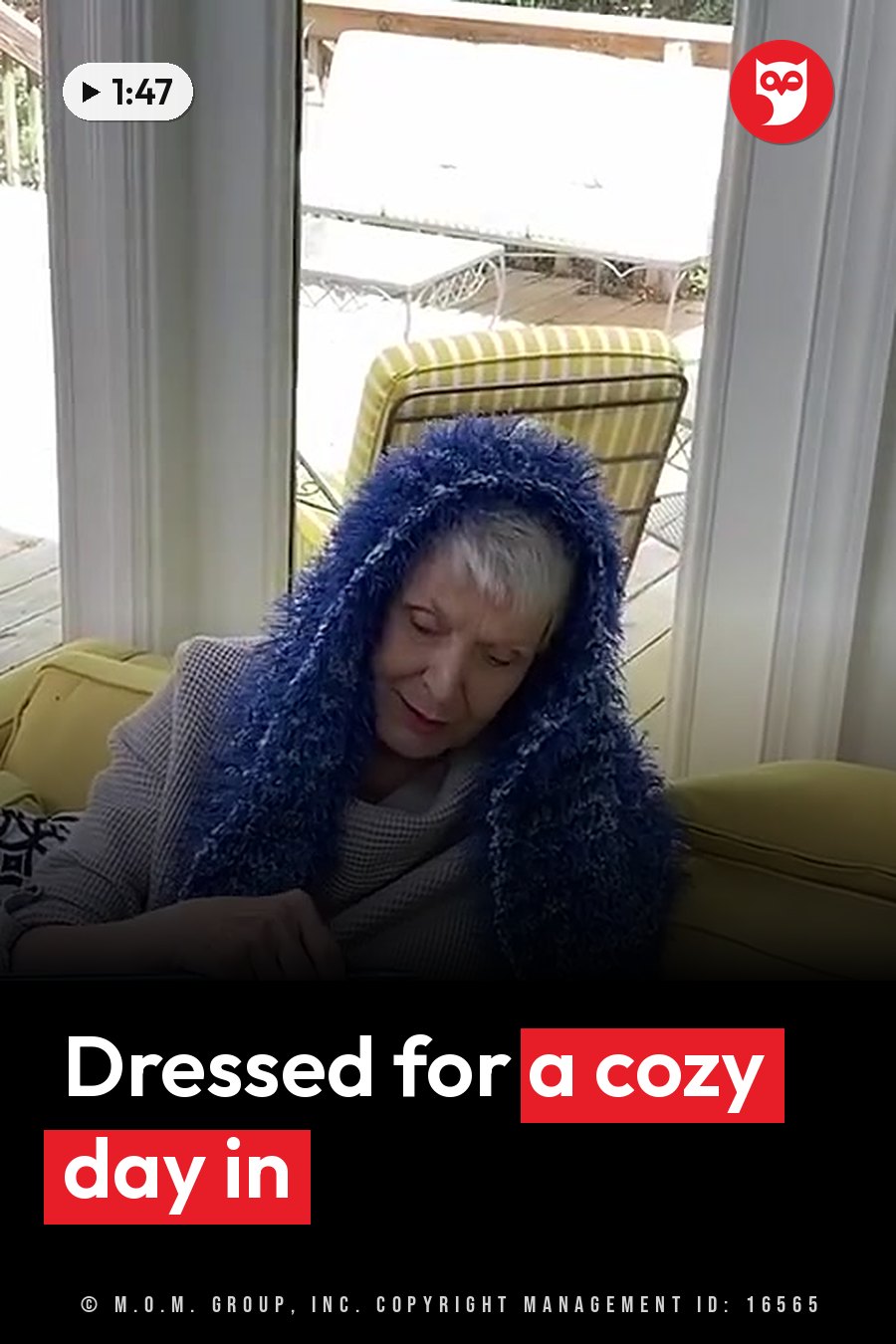 An older woman in a blue fuzzy hooded scarf sits on a yellow couch and looks down. A headline runs in white letters across the lower third.