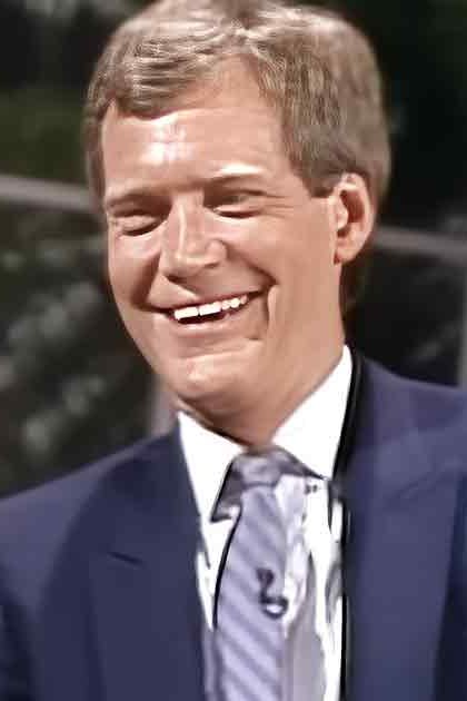 Two adults, an older male and a younger male, wearing formal suits from the mid-20th century, seated in what appears to be a television studio setup with professional lighting.