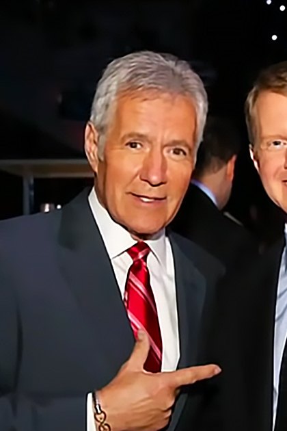 Two adult men in formal attire, one with gray hair and a red striped tie, another with brown hair and a patterned tie, standing indoors at an evening event space.