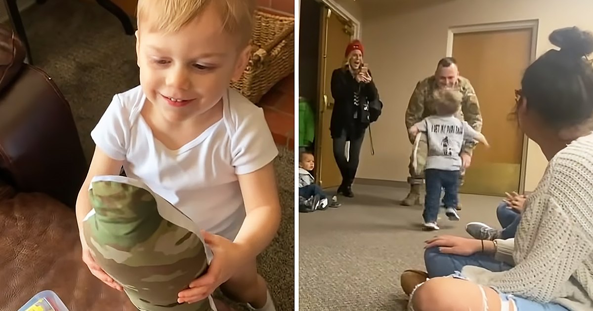 Indoors, young child wearing a white cotton T-shirt with 'I got my daddy back' text holding camouflage-patterned item, surrounded by adults dressed in winter and military attire, carpeted floor, artificial lighting, evening or night setting.