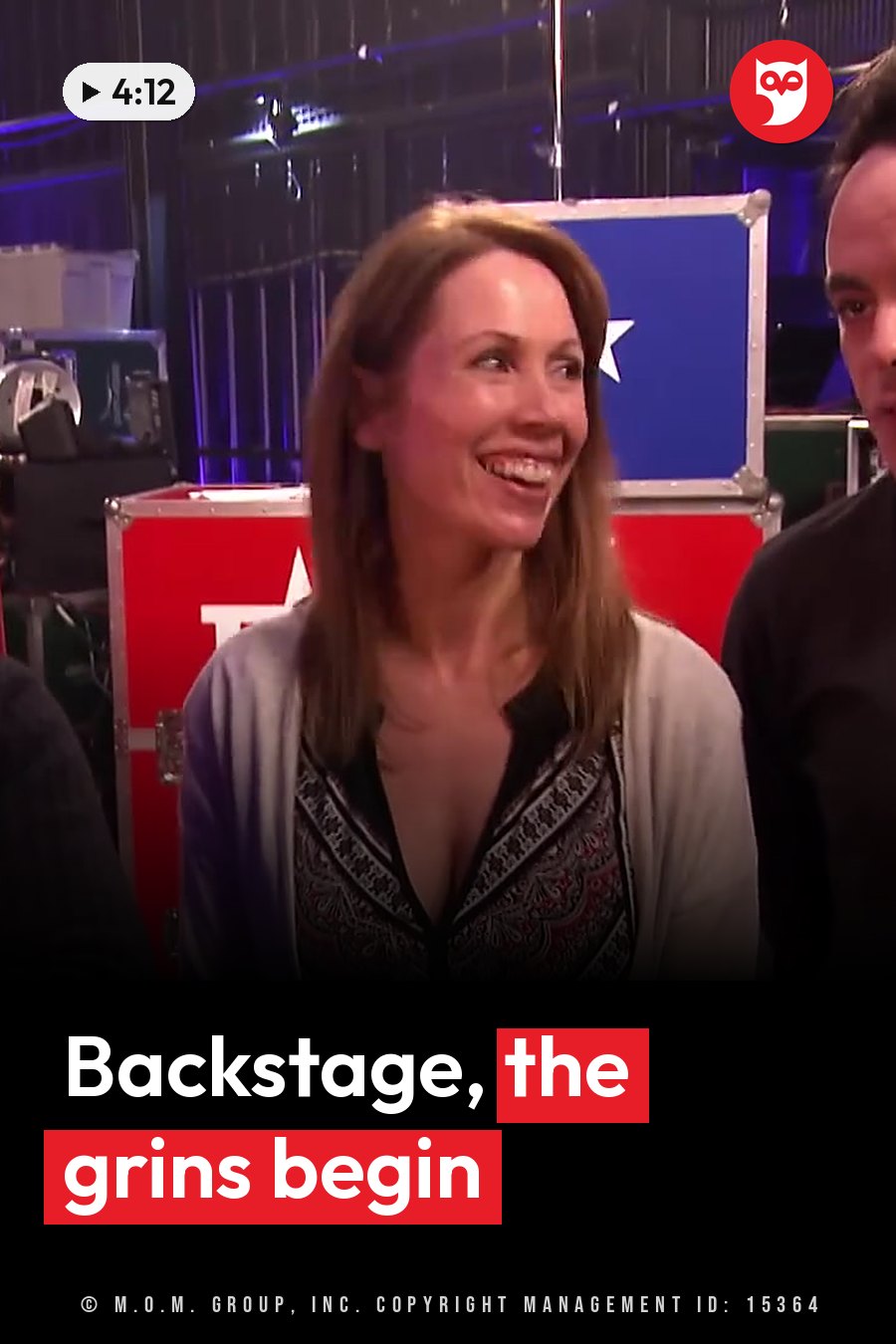 A woman smiles and looks to her right, standing beside a man near stacks of colorful equipment cases. A headline runs in white letters across the lower third.