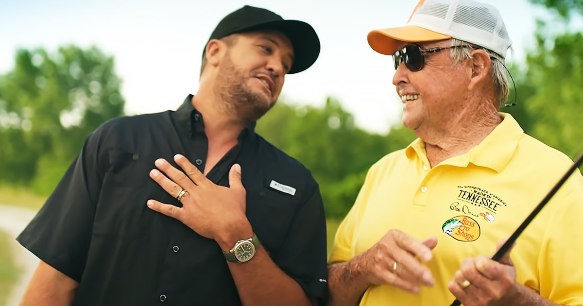 Middle-aged men in a park, one wearing a black button-up shirt with 'Tennessee' branding and the other in a yellow polo shirt holding what appears to be a fishing rod.