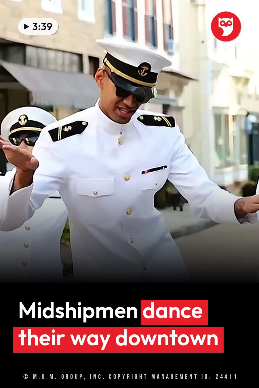 Two men in white naval uniforms, hats and sunglasses dance on a street near buildings. A headline runs in white letters across the lower third.
