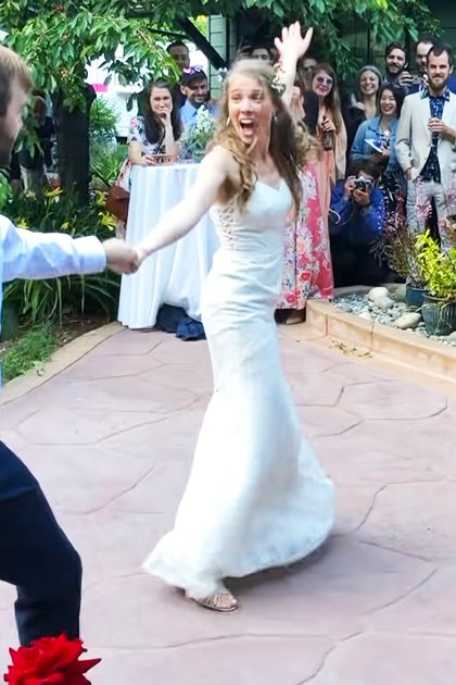 An outdoor wedding reception with a couple dancing joyfully in a garden courtyard surrounded by stone pathways and greenery.