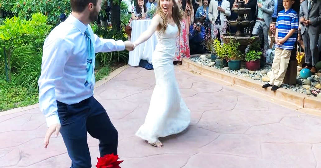 An outdoor wedding reception with a couple dancing joyfully in a garden courtyard surrounded by stone pathways and greenery.