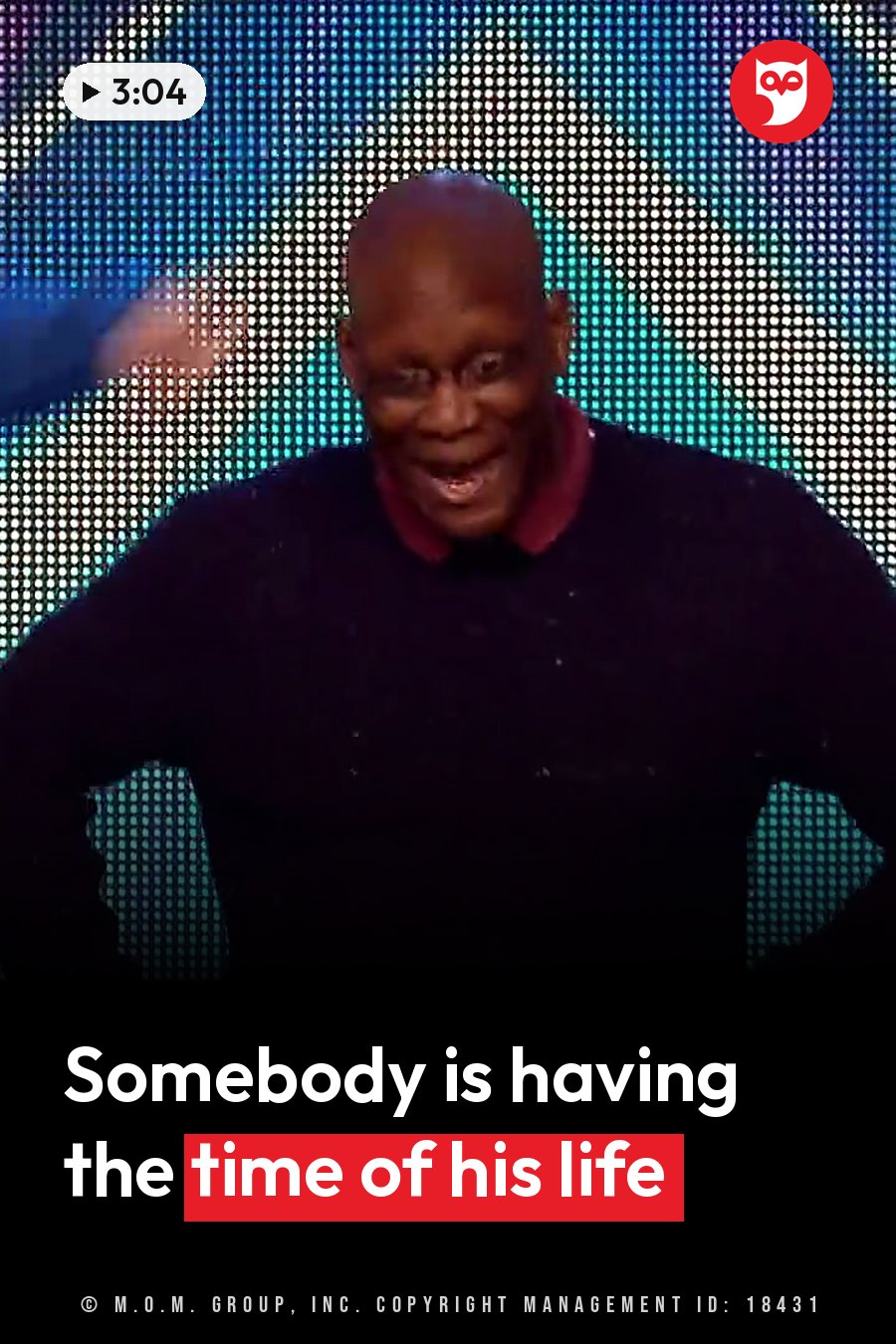 A bald man with glasses smiles broadly. He wears a dark sweater over a red collared shirt. A headline runs in white letters across the lower third.