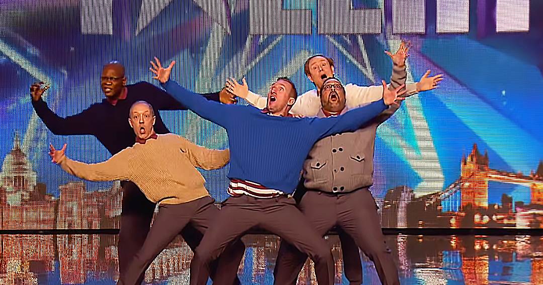 Group performing on stage with a cityscape backdrop at 'Britain's Got Talent' event.