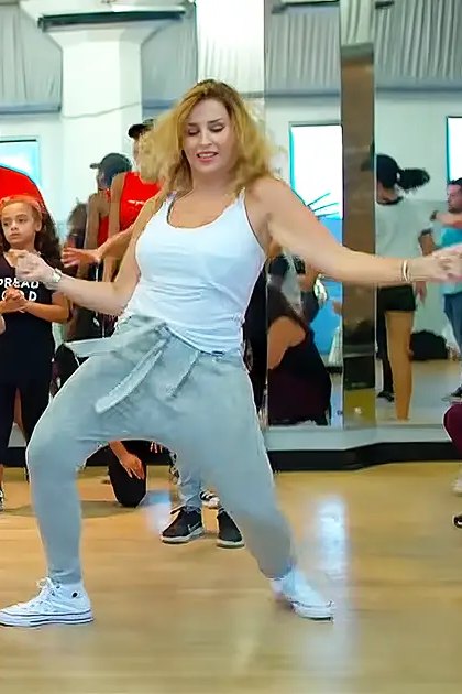 A dance class in progress at a fitness studio with various participants and mirrors reflecting the scene.
