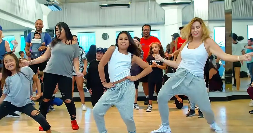 A dance class in progress at a fitness studio with various participants and mirrors reflecting the scene.