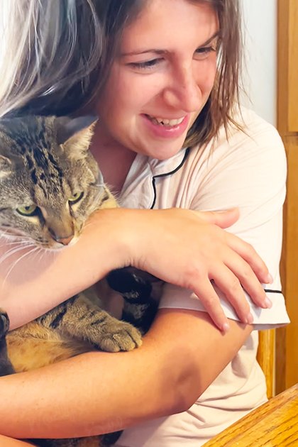 Young adult female in a casual indoor setting with wooden furniture and a green parrot, light natural lighting, and soft colors like brown, cream, and green.