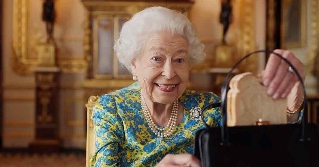 An older adult female wearing a blue and yellow floral dress with pearl jewelry, holding a black handbag, set against opulent grand palace decor.