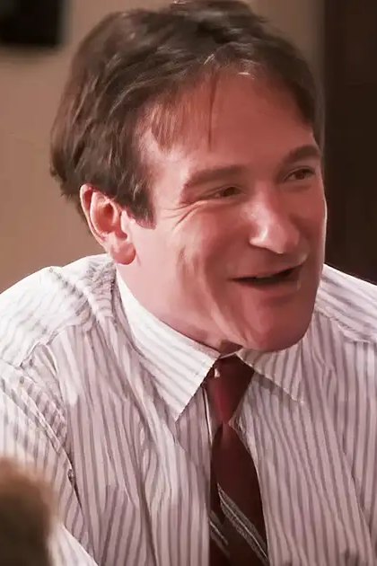 An adult male in a home setting, wearing a white shirt with thin vertical stripes and a dark tie, suggesting formal or semi-formal attire.