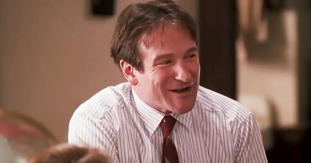 An adult male in a home setting, wearing a white shirt with thin vertical stripes and a dark tie, suggesting formal or semi-formal attire.