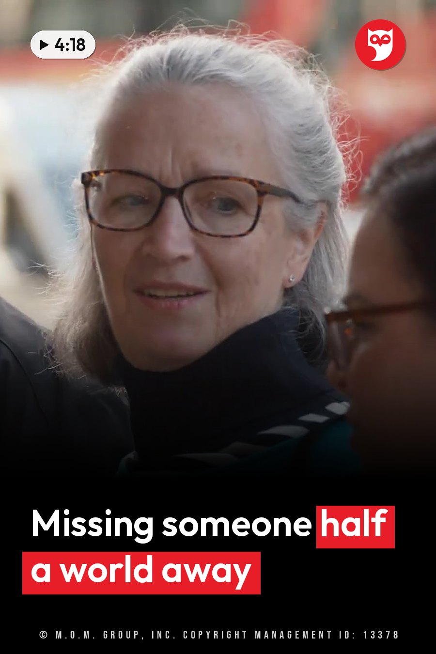 An older woman with gray hair and glasses speaks while another person listens nearby. A headline runs in white letters across the lower third.
