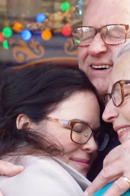 A family reunion with festive decorations indoors, with an older adult male and two older females smiling amidst holiday lights and a carousel-like structure.