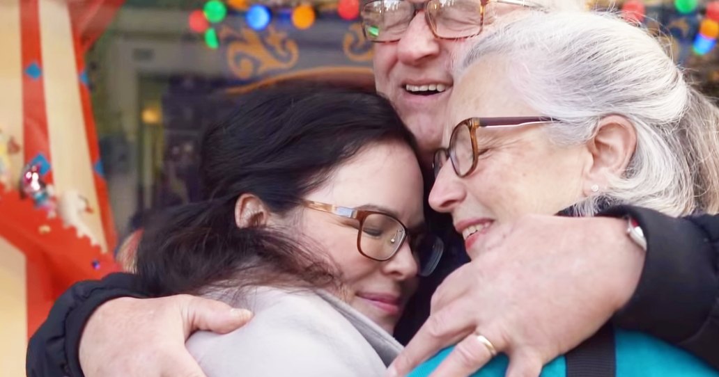 A family reunion with festive decorations indoors, with an older adult male and two older females smiling amidst holiday lights and a carousel-like structure.