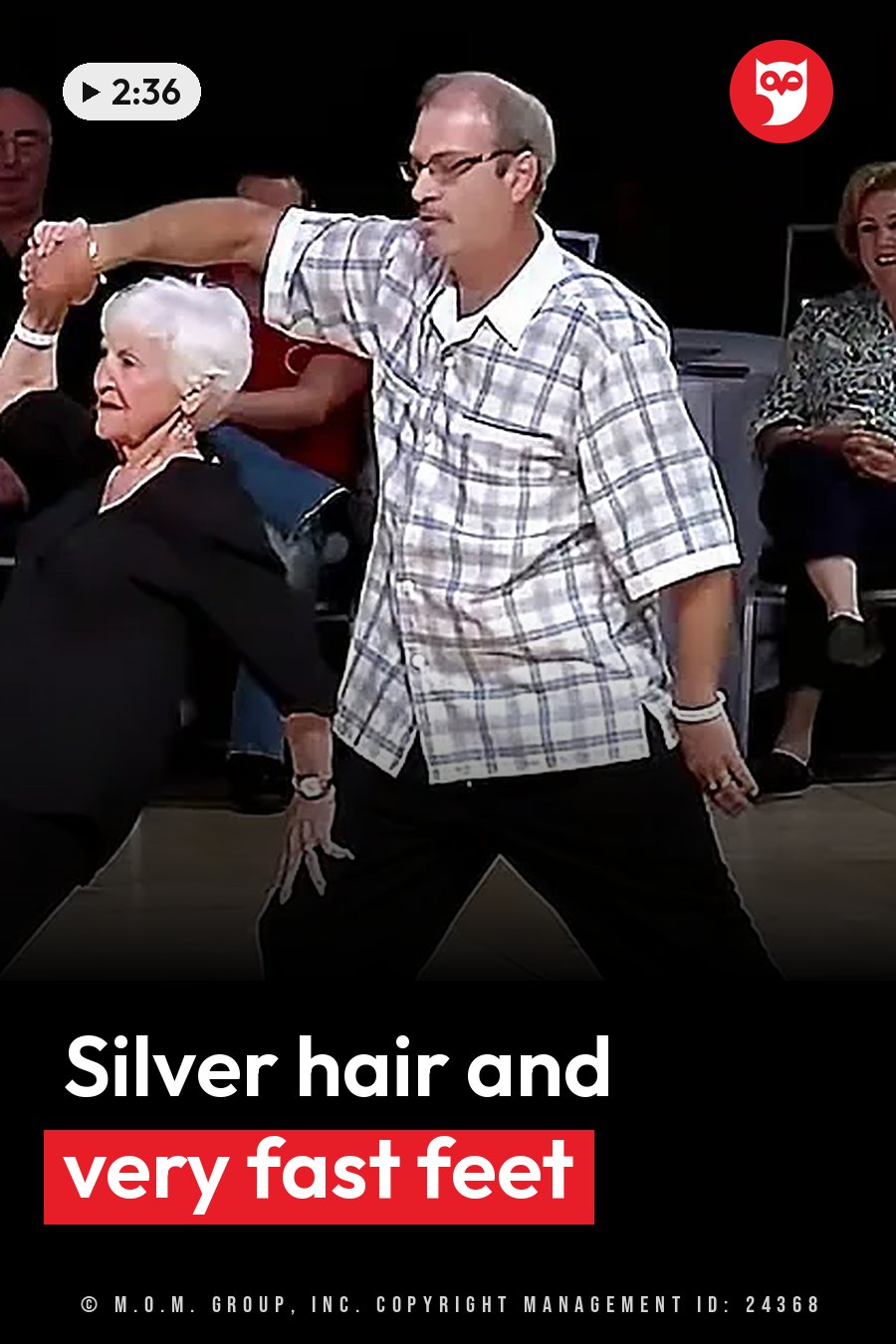 An older man and woman dance together on a stage while people watch from seats. A headline runs in white letters across the lower third.