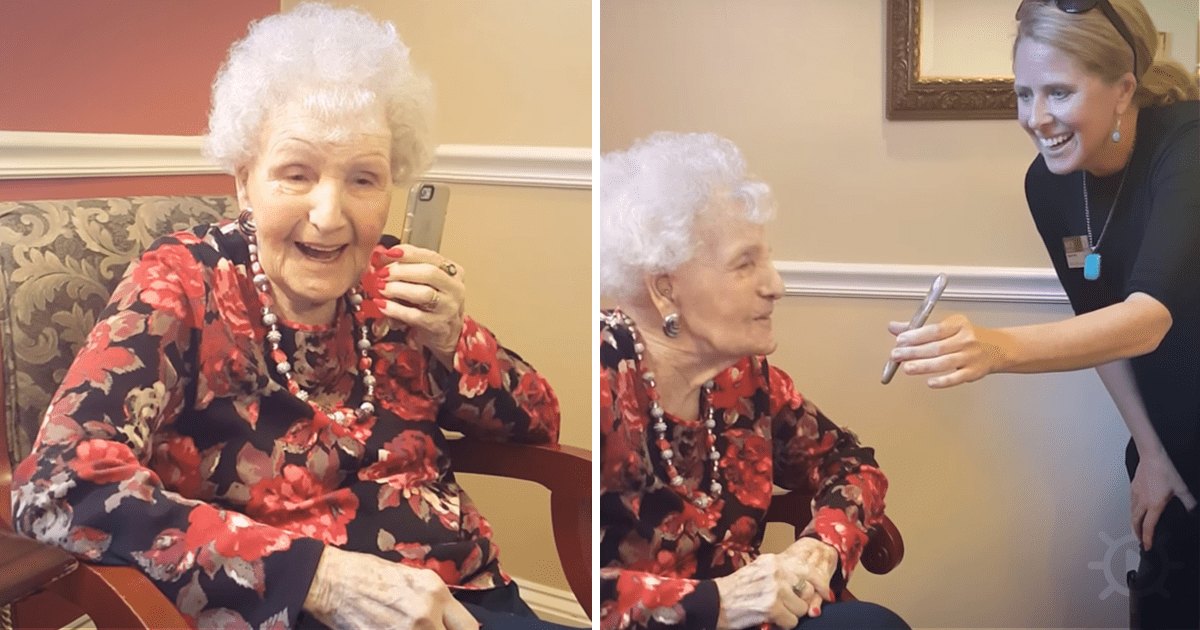 An older adult woman in a floral blouse with red flowers, sitting on an ornate chair indoors at a nursing home. A younger adult staff member is present nearby.