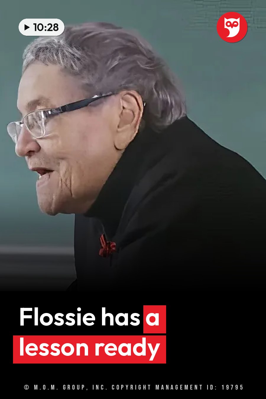 An older woman with glasses and gray hair, in a black jacket with a red pin, speaks. A headline runs in white letters across the lower third.