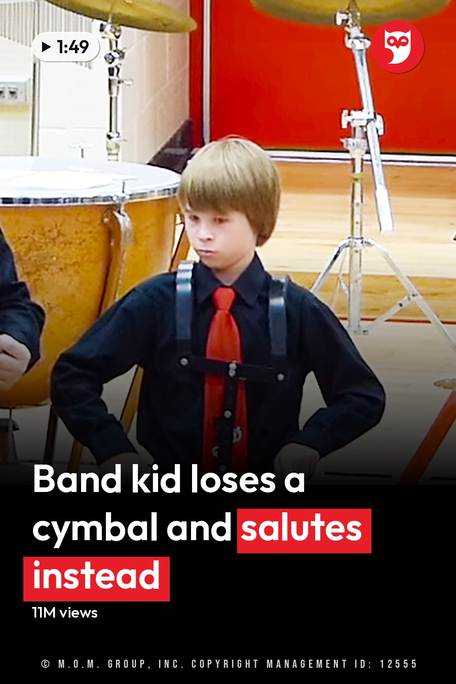 Children playing drums inside a school gymnasium with wooden floors and white-red walls, wearing black shirts with red ties and black pants; drumsticks visible. The headline runs in white letters across the lower third.