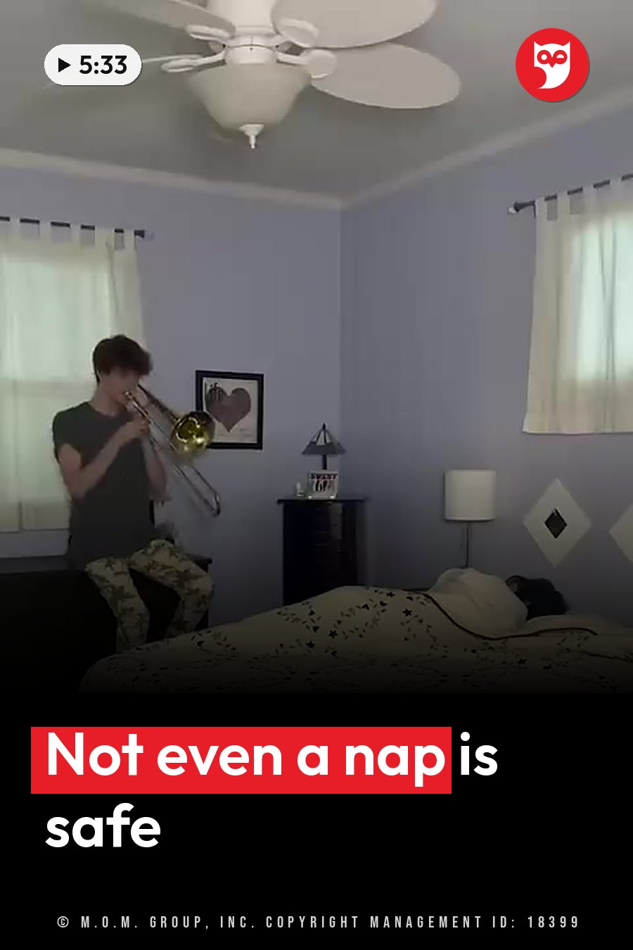A person plays a trombone beside someone asleep on a bed, in a room with a ceiling fan and curtains. A headline runs in white letters across the lower third.