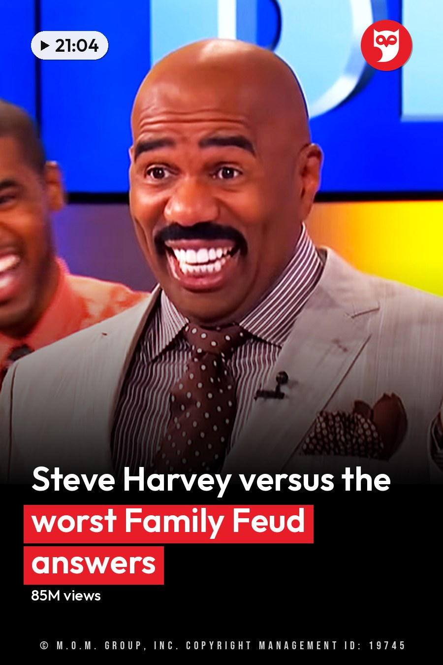 A man in his adult years wearing a light gray suit jacket with a striped shirt and polka dot tie stands on a television show set, surrounded by other adults engaged in dialogue. The headline runs in white letters across the lower third.