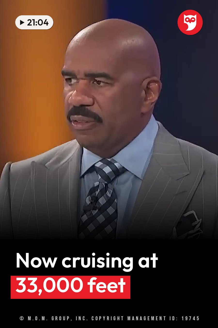 Steve Harvey, a bald man with a mustache, wears a gray suit, blue shirt and checkered tie while speaking. A headline runs in white letters across the lower third.