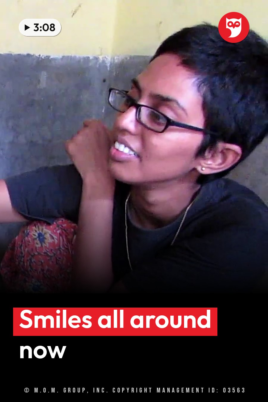 A person with short dark hair and glasses smiles, chin resting on one hand, against a two-toned wall. A headline runs in white letters across the lower third.