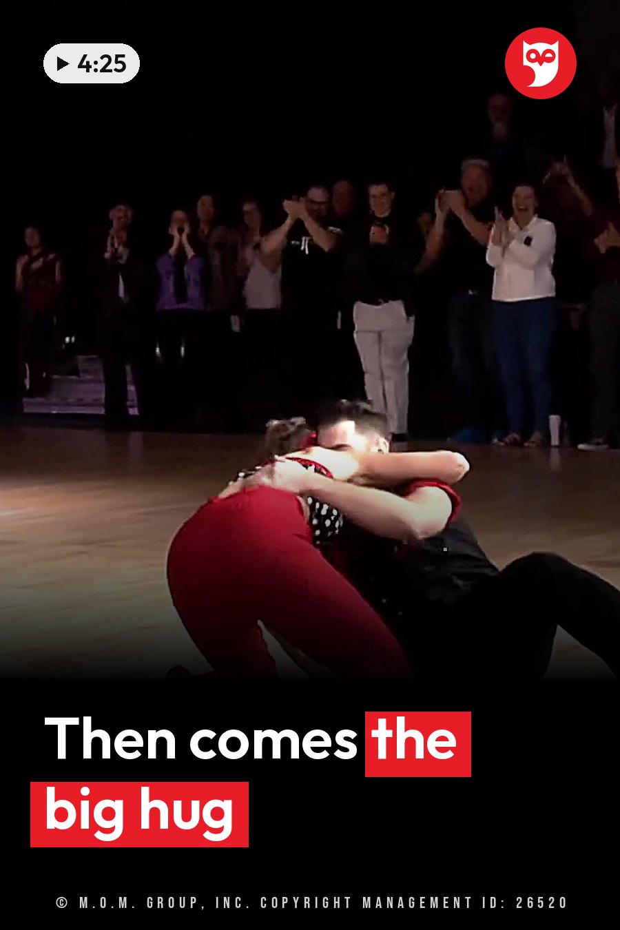 Two dancers embrace on a stage while an audience claps behind them. A headline runs in white letters across the lower third.