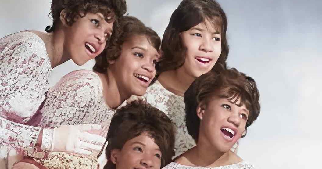 A family group in an indoor setting; children wearing similar floral-patterned dresses against a plain background