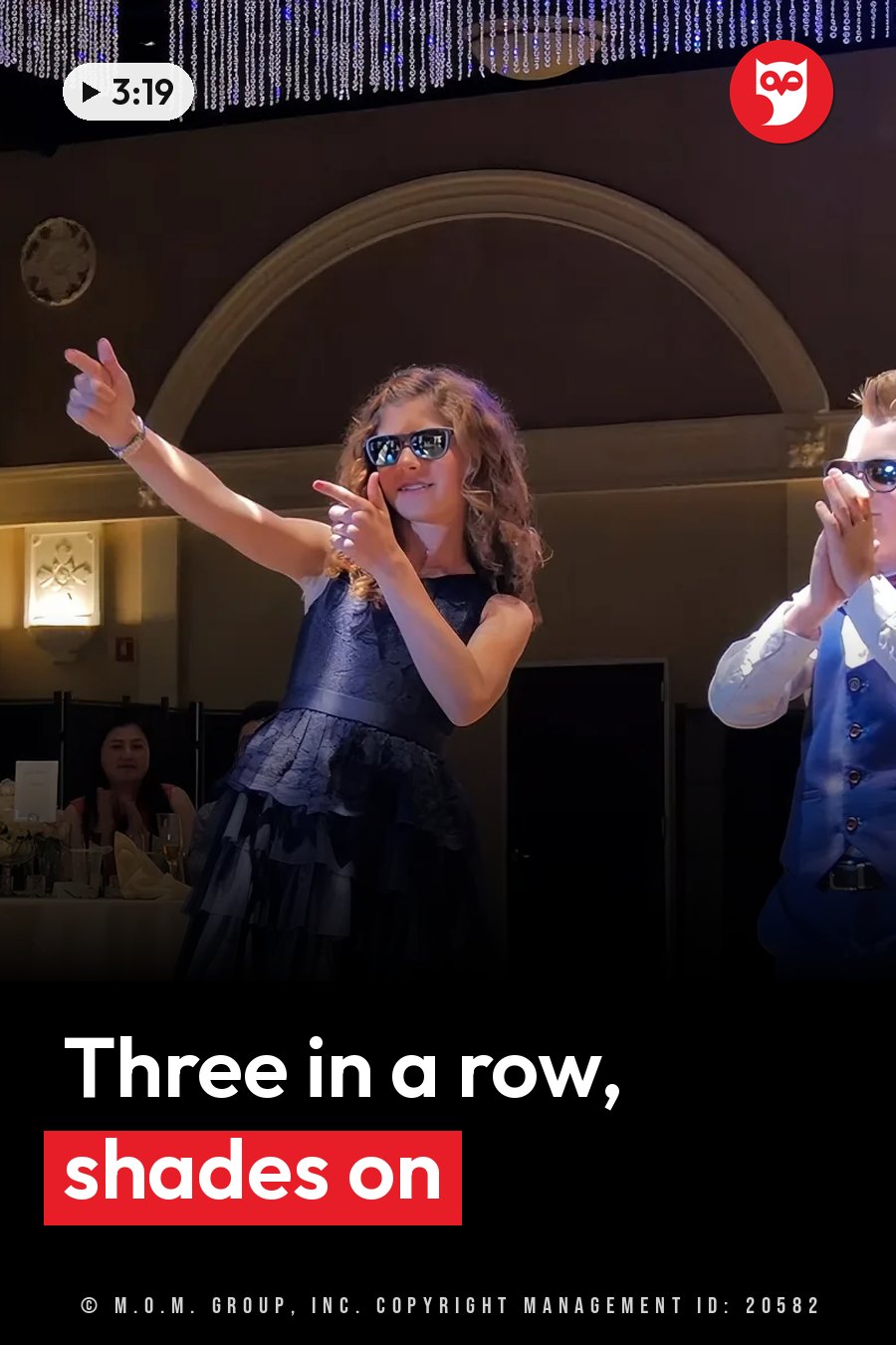 A girl in a dark dress and sunglasses points with both hands beside a boy who also wears sunglasses. A headline runs in white letters across the lower third.