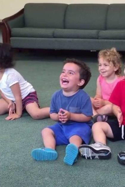 Group of children in an indoor setting, wearing casual clothing; green sofa with cushions, wooden side tables, and a casual environment.