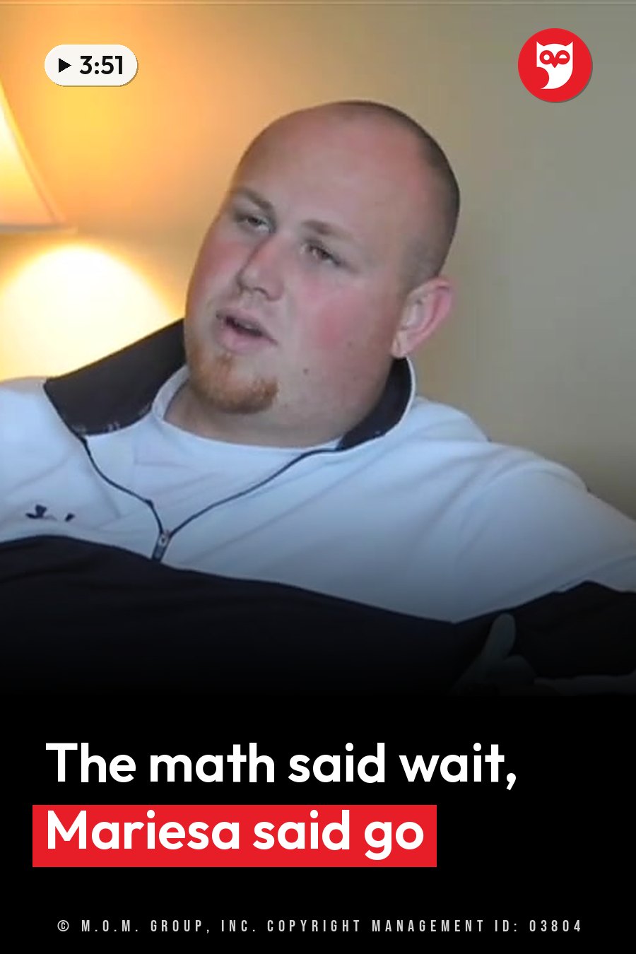 A bald man with a goatee, wearing a white zip-up jacket, sits indoors and talks. A headline runs in white letters across the lower third.