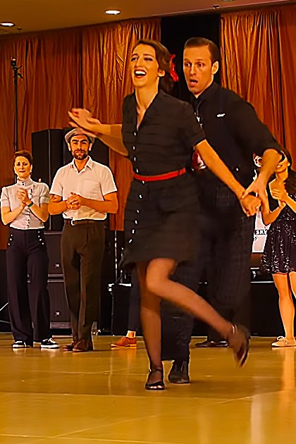 A couple dancing swing in front of an audience at the International Lindy Hop Championships 2021, with a banner reading 'International Lindy Hop Championships,' curtains, and microphones visible.
