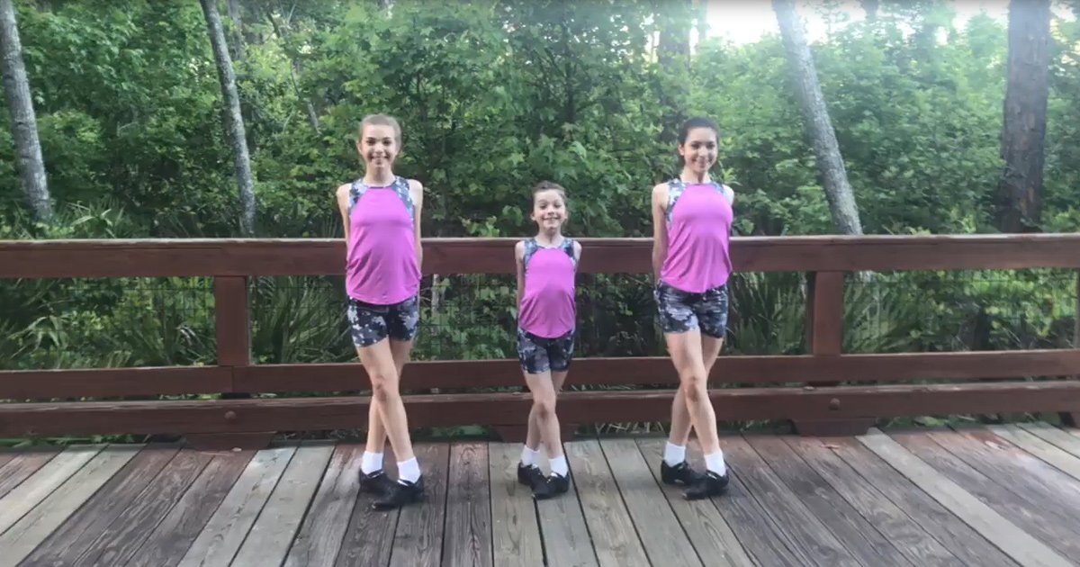 Three young female children in a wooded outdoor setting with lush greenery and natural light filtering through the trees.