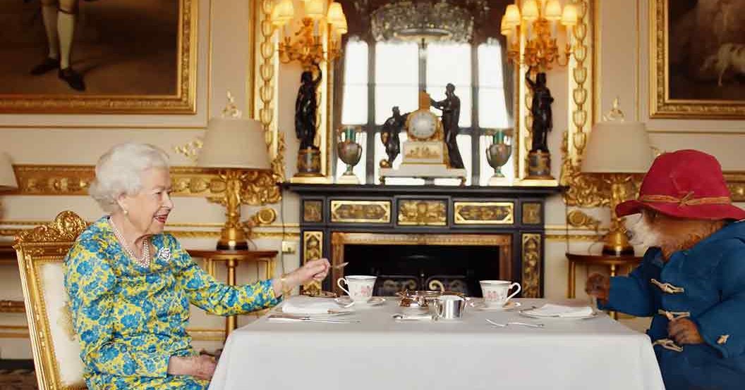 Opulent room with ornate gold-framed chairs, framed paintings on walls, and chandeliers at Buckingham Palace during daytime with natural light.