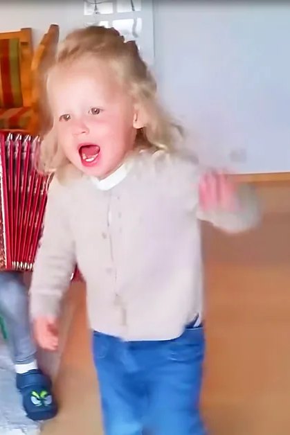 Two toddlers, a boy and girl, dressed casually indoors, holding an accordion.