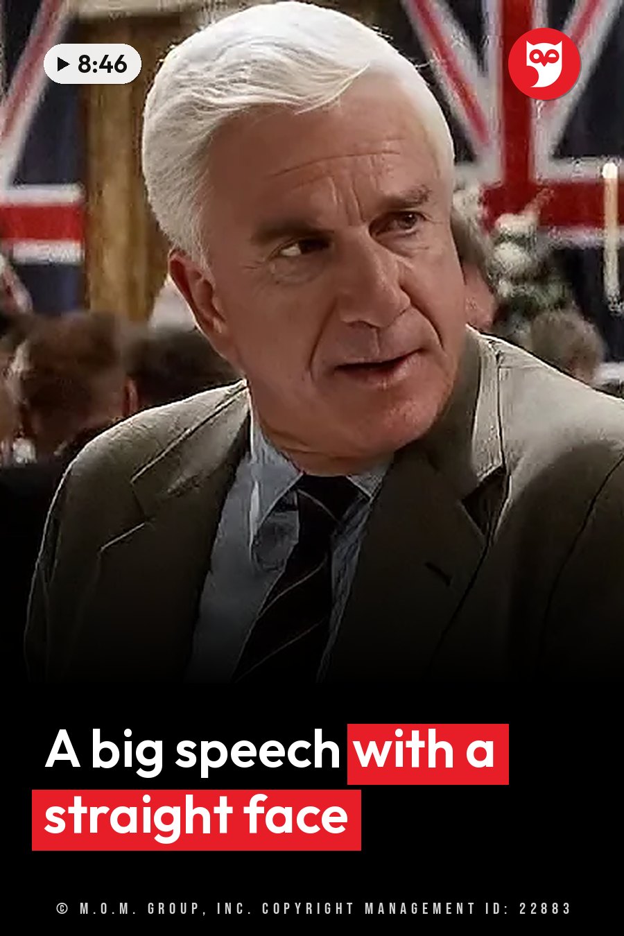 An older man with white hair, in a suit and tie, looks ahead as he speaks at an event near a flag. A headline runs in white letters across the lower third.