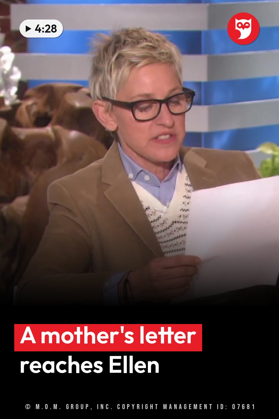 A person with short hair and glasses holds a paper and speaks, wearing a jacket over a patterned sweater. A headline runs in white letters across the lower third.